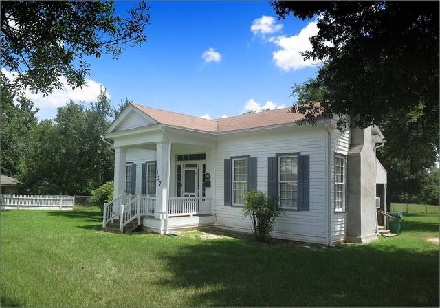 White clapboard cottage with a covered front porch on a green lawn